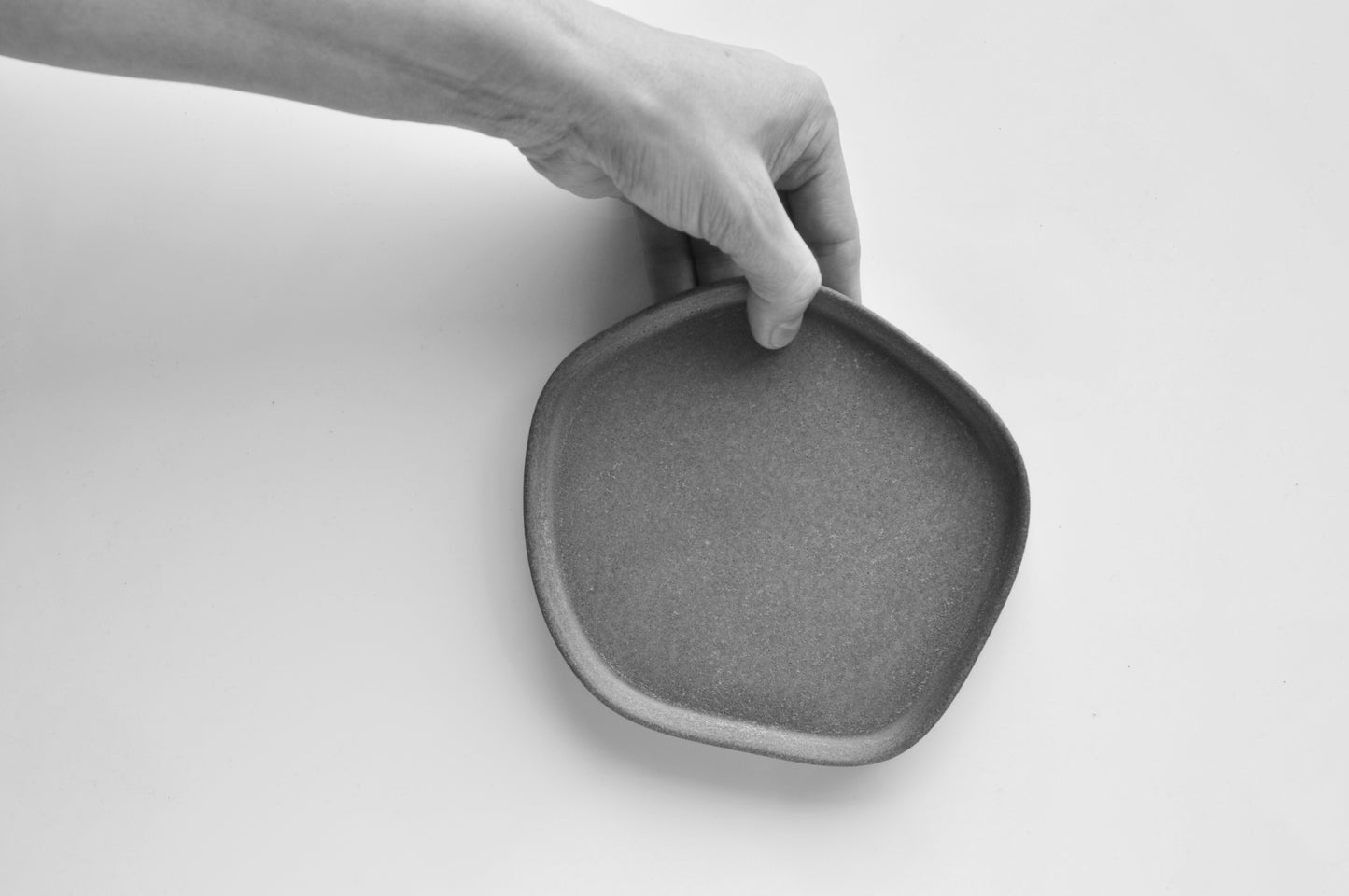 Hand holding a gray concrete plate on a white background