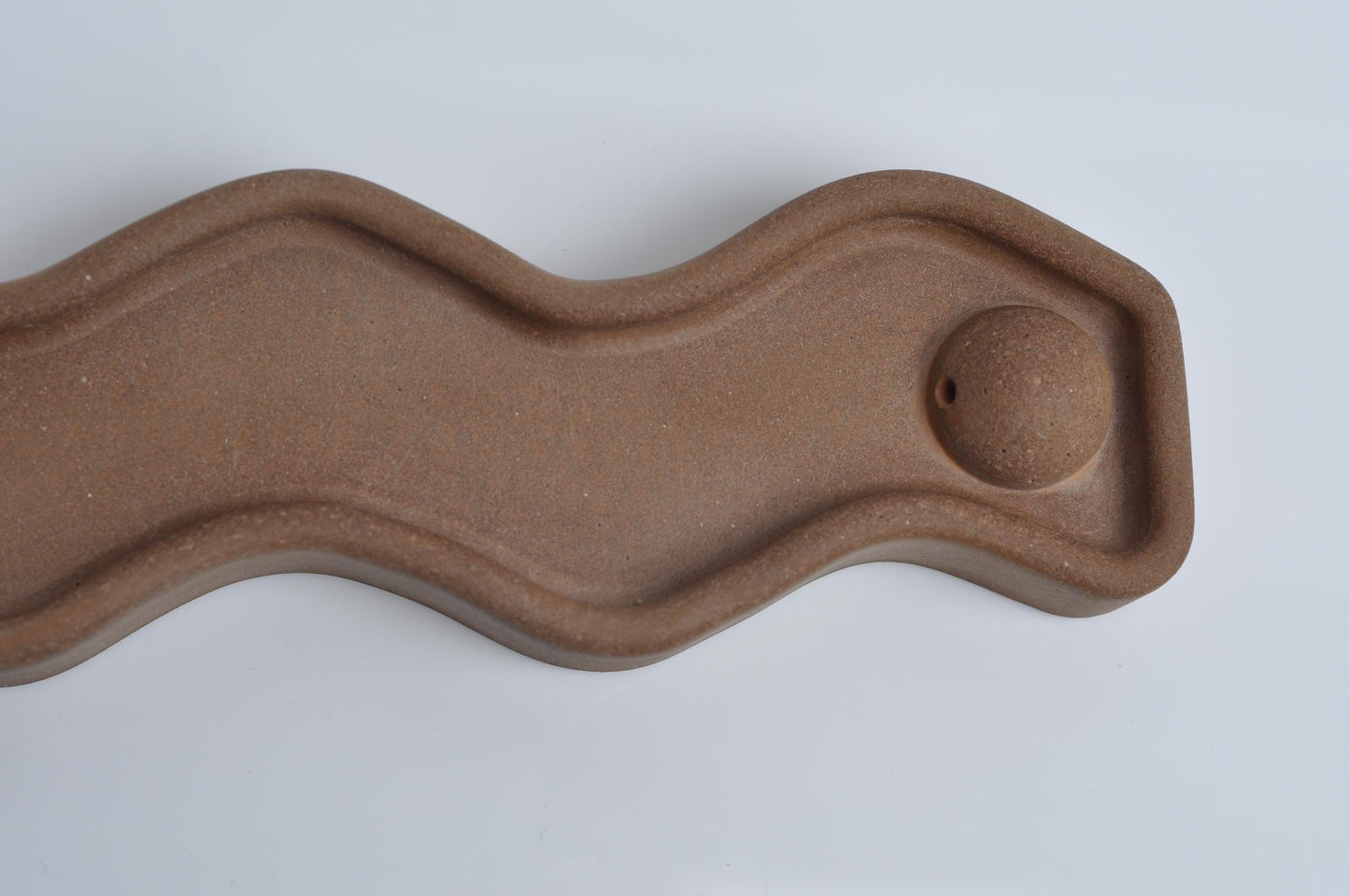 Brown cement incense holder with wavy design on a white background