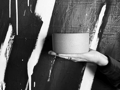 Person holding a cylindrical concrete object against a textured black and white background