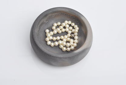 Pearl necklace on a dark gray ceramic dish against a light gray background