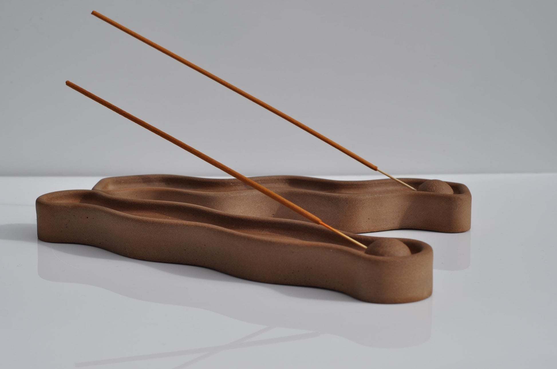Brown concrete incense holder with two sticks on a light gray background