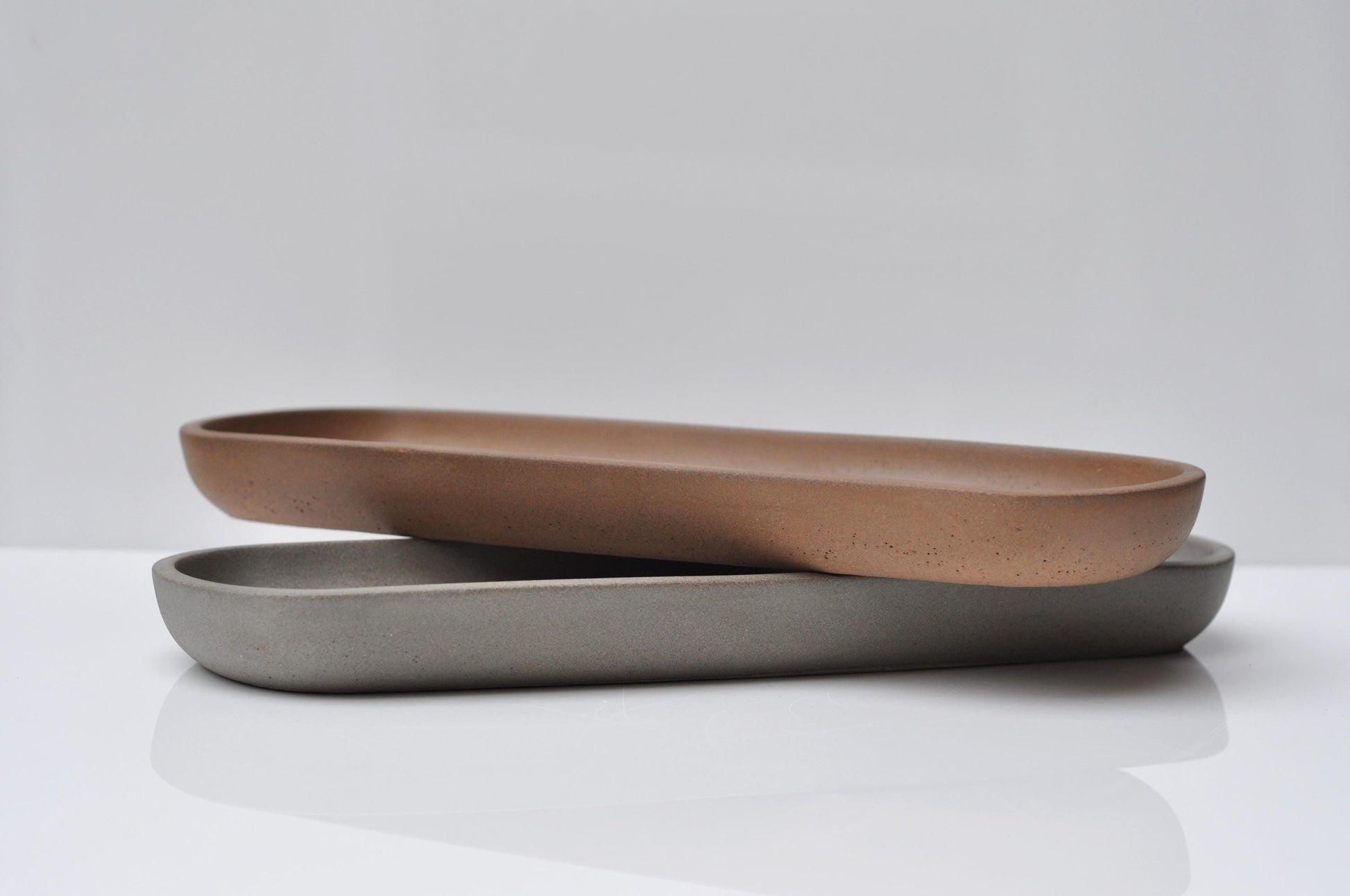 Two oval trays, one brown and one gray, on a white surface with a light gray background.