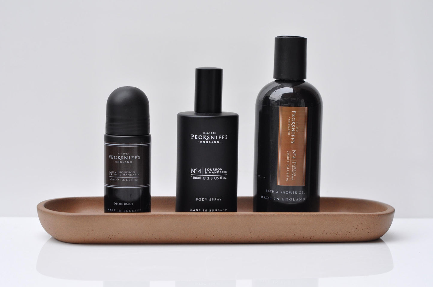 Four bottles of Feenicks & Co. products on a concrete tray with a white background