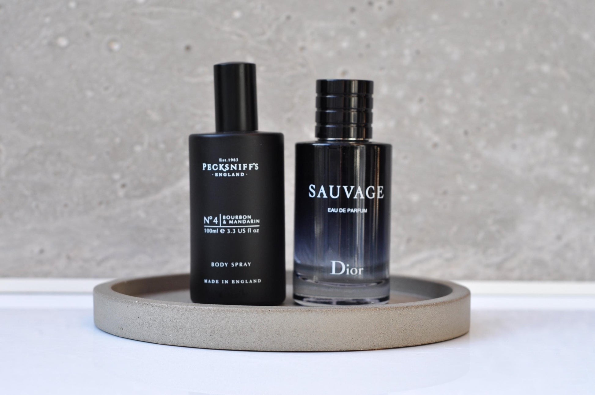 Two bottles of men's grooming products on a gray tray with a neutral background