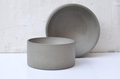 Two gray cement bowls on a white surface with a light gray textured background