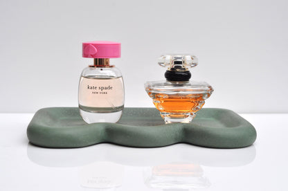 Two perfume bottles on a decorative green tray with a white background