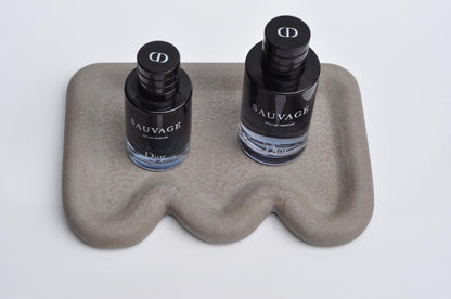 Two bottles of Dior Sauvage cologne on a wavy stone surface with a white background