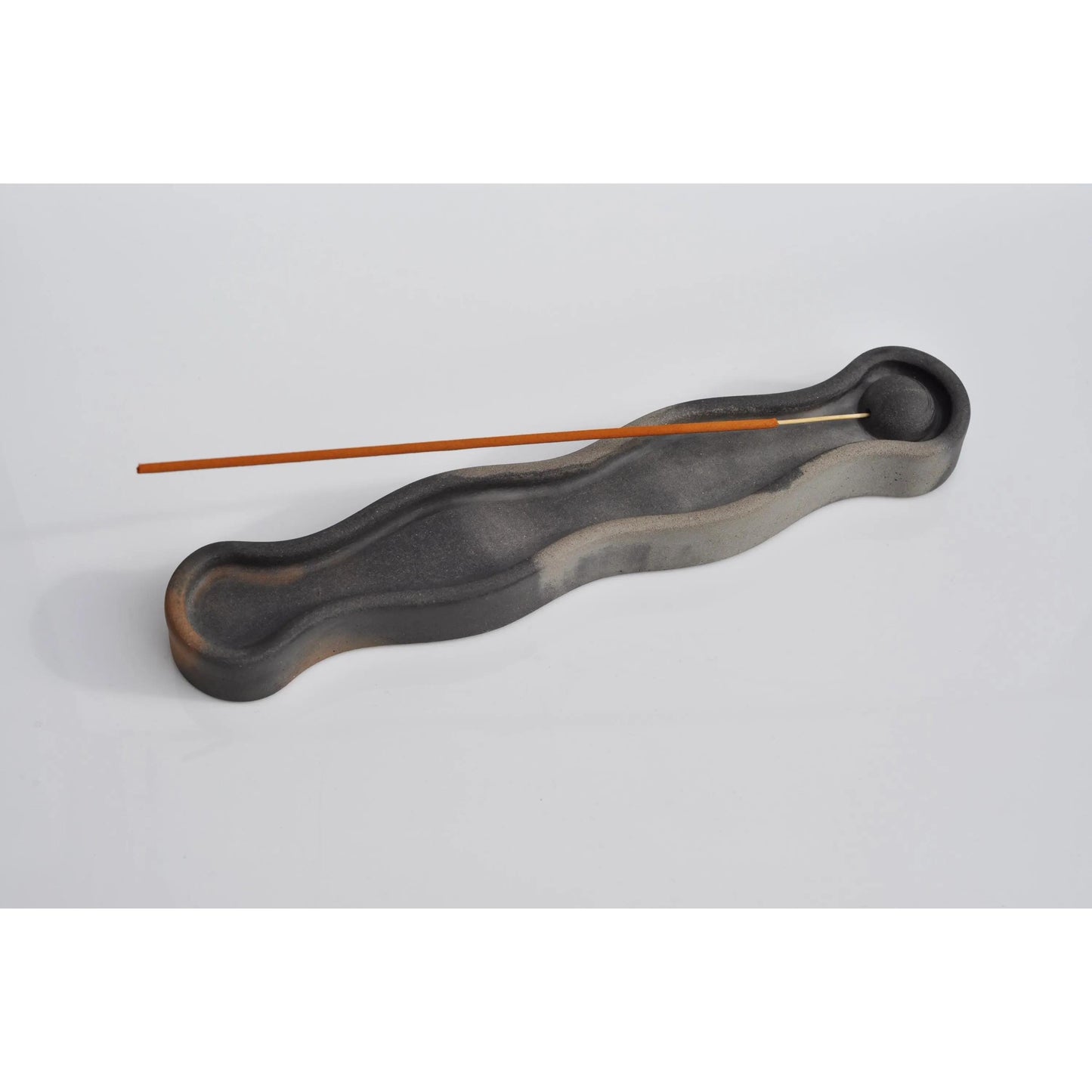 Black wavy incense holder with two sticks on a light gray background