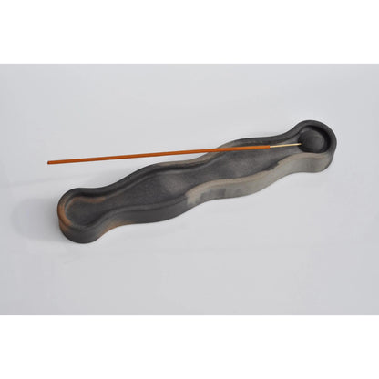 Black wavy incense holder with two sticks on a light gray background