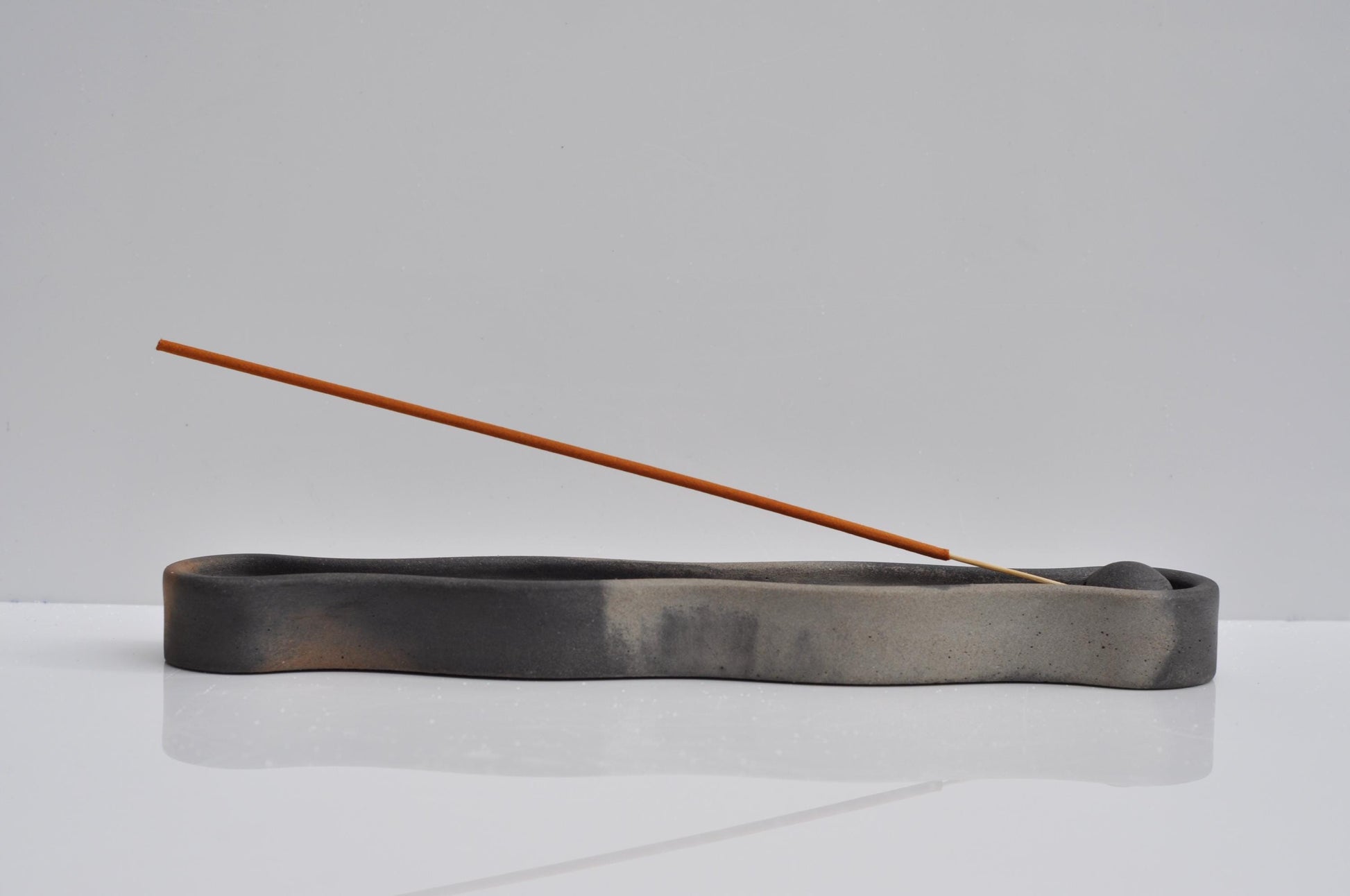 Incense burner with a single incense stick on a light gray background