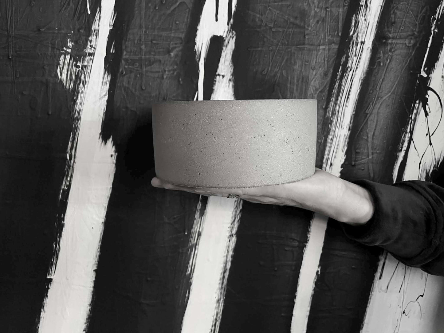Person holding a cylindrical concrete object against a textured black and white background