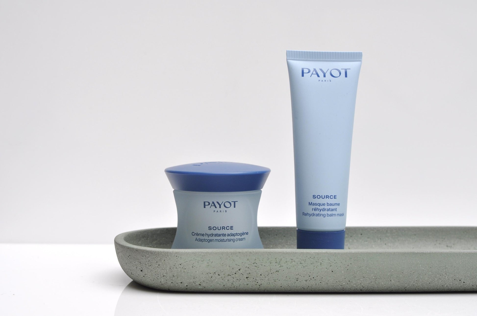 Two Payot skincare products on a gray tray with a white background