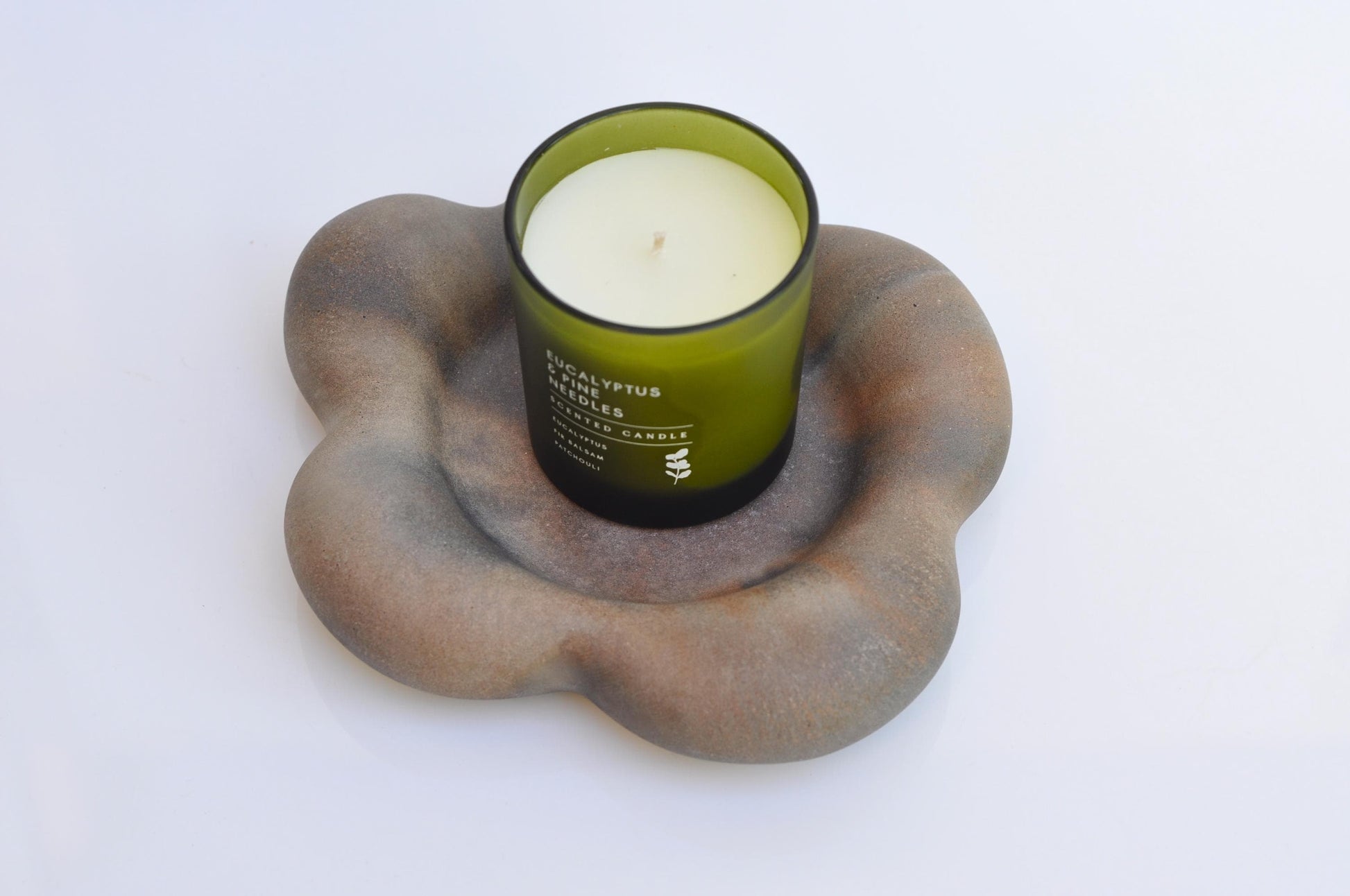 Candle in a green holder on a textured stone-like surface with a white background