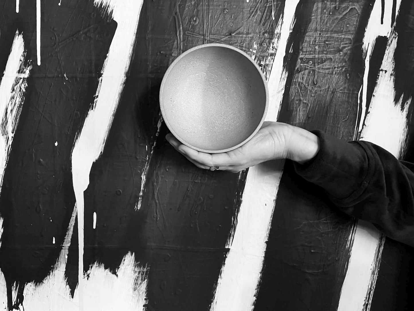 Hand holding a cement bowl against a black and white abstract background