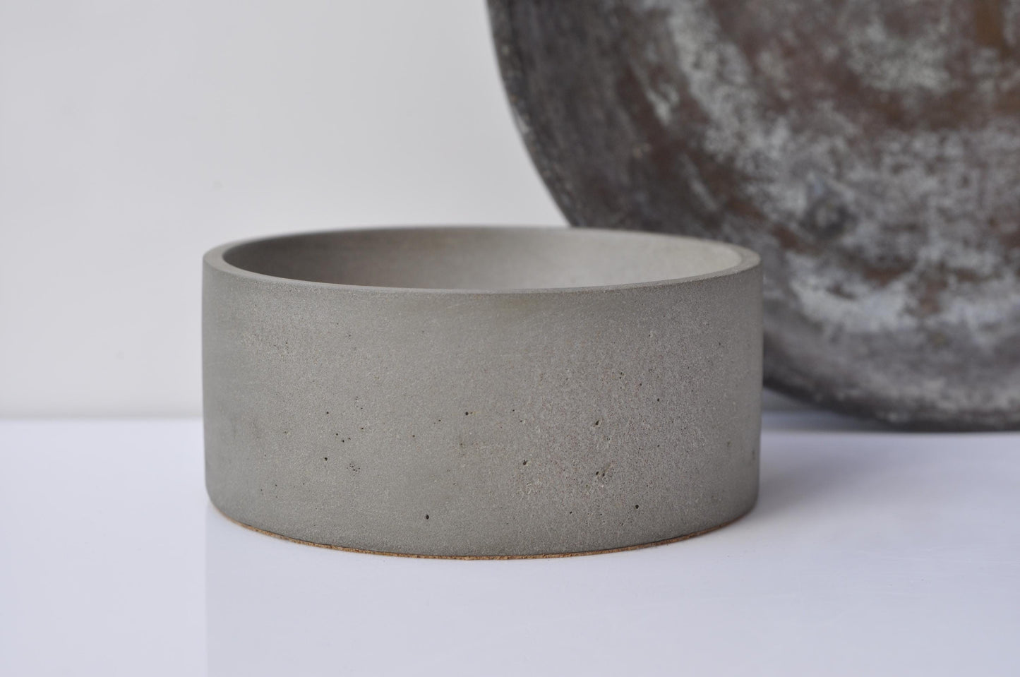 Concrete bowl on a white surface with a blurred textured object in the background