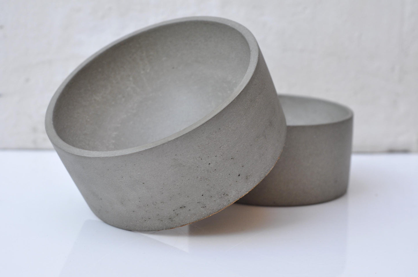 Two concrete bowls on a white surface with a neutral background