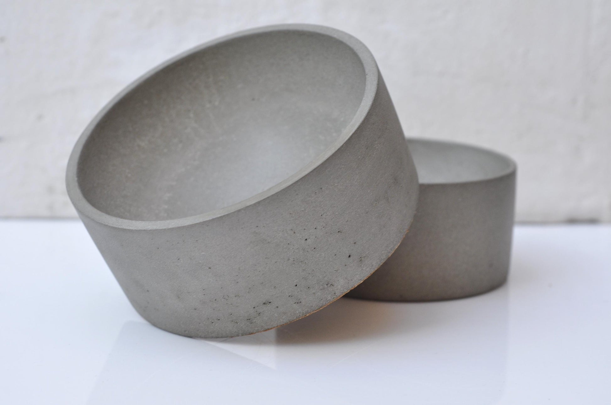 Two concrete bowls on a white surface with a neutral background