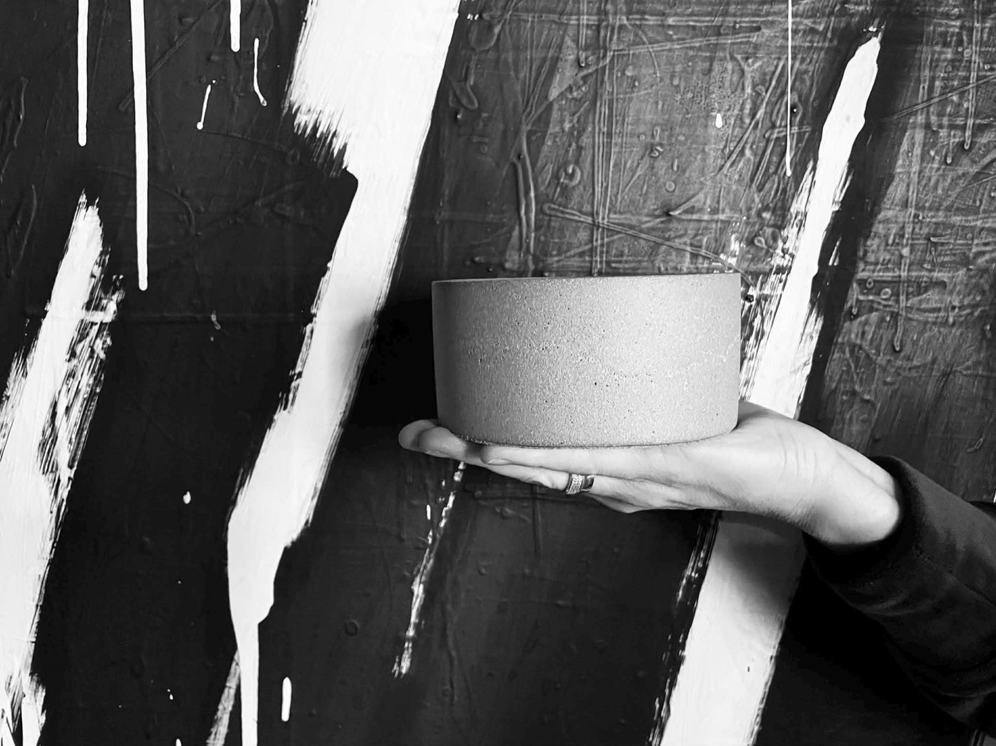 Person holding a cylindrical concrete object against a textured black and white background