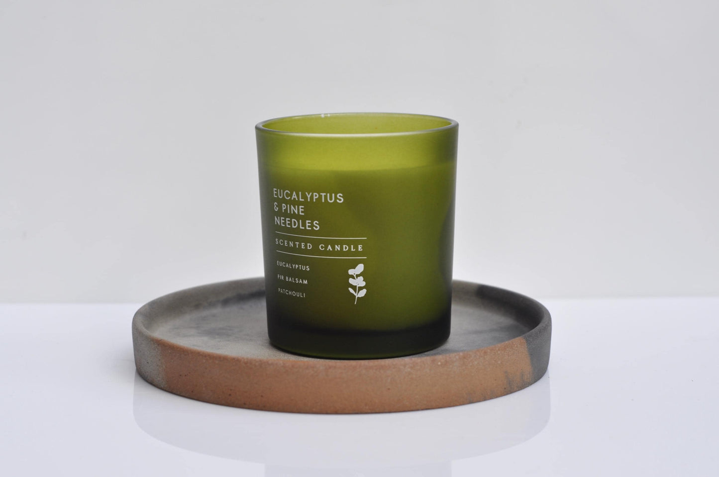 Green candle labeled 'Eucalyptus & Pine Needles' on a concrete coaster with a white background