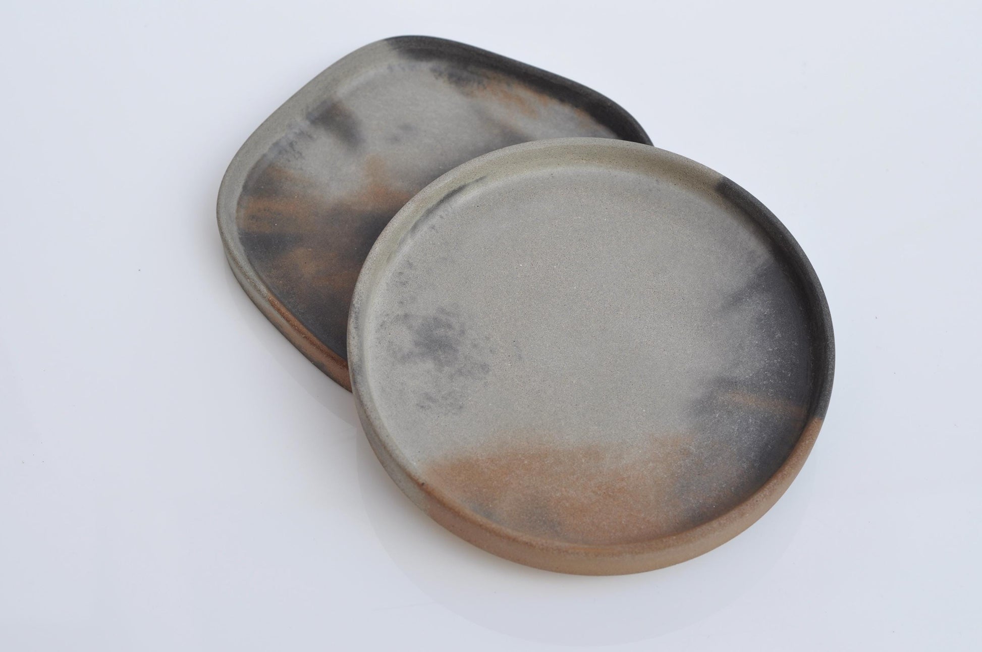 Two round concrete trays with a brownish-black rim on a white background