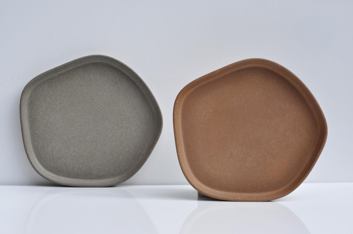 Two cement plates, one gray and one brown, on a white surface with a light gray background.
