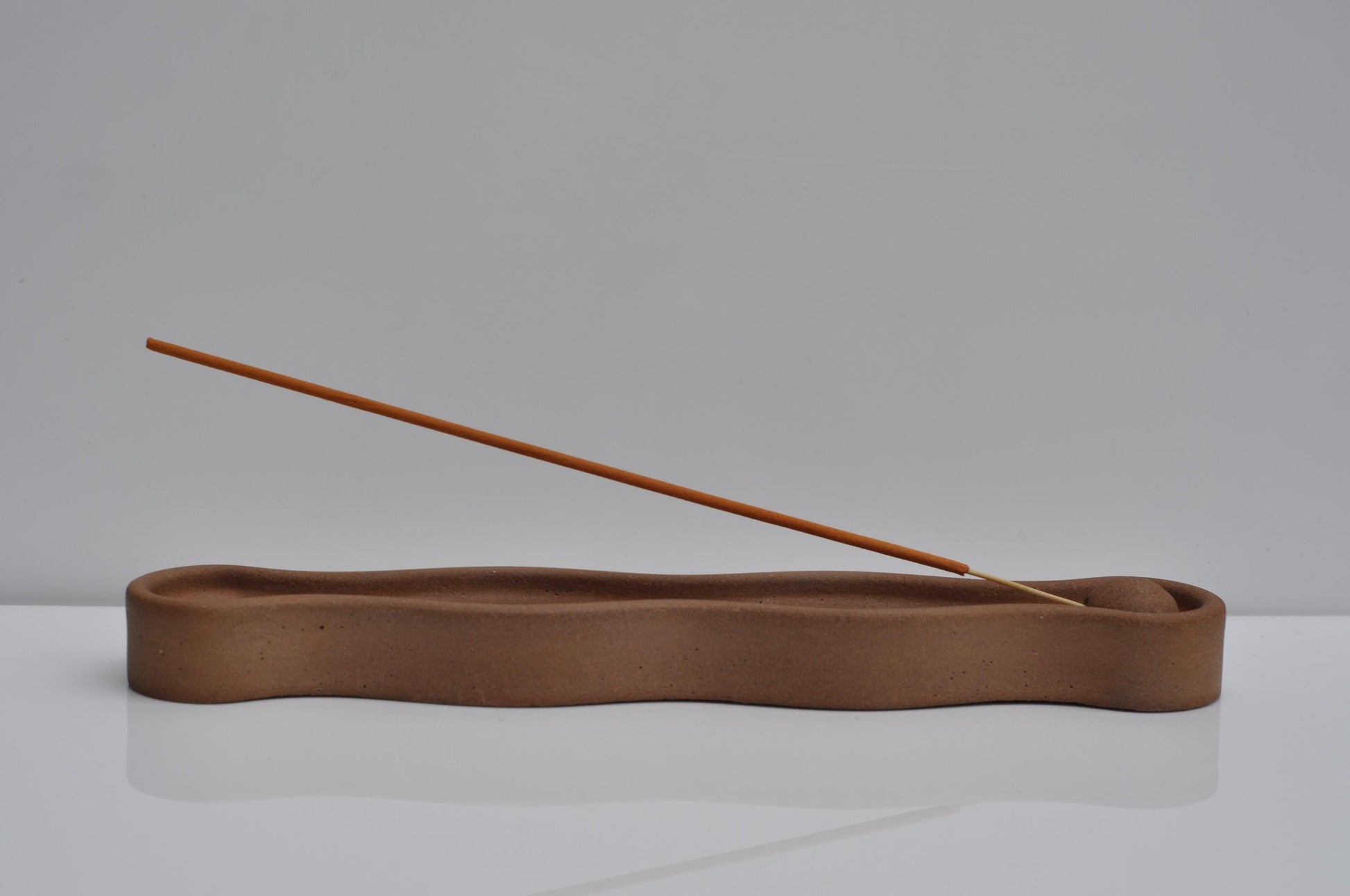 Brown wavy incense holder with a wooden stick on a gray background