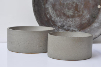 Two gray cement bowls on a white surface with a textured metal object in the background.