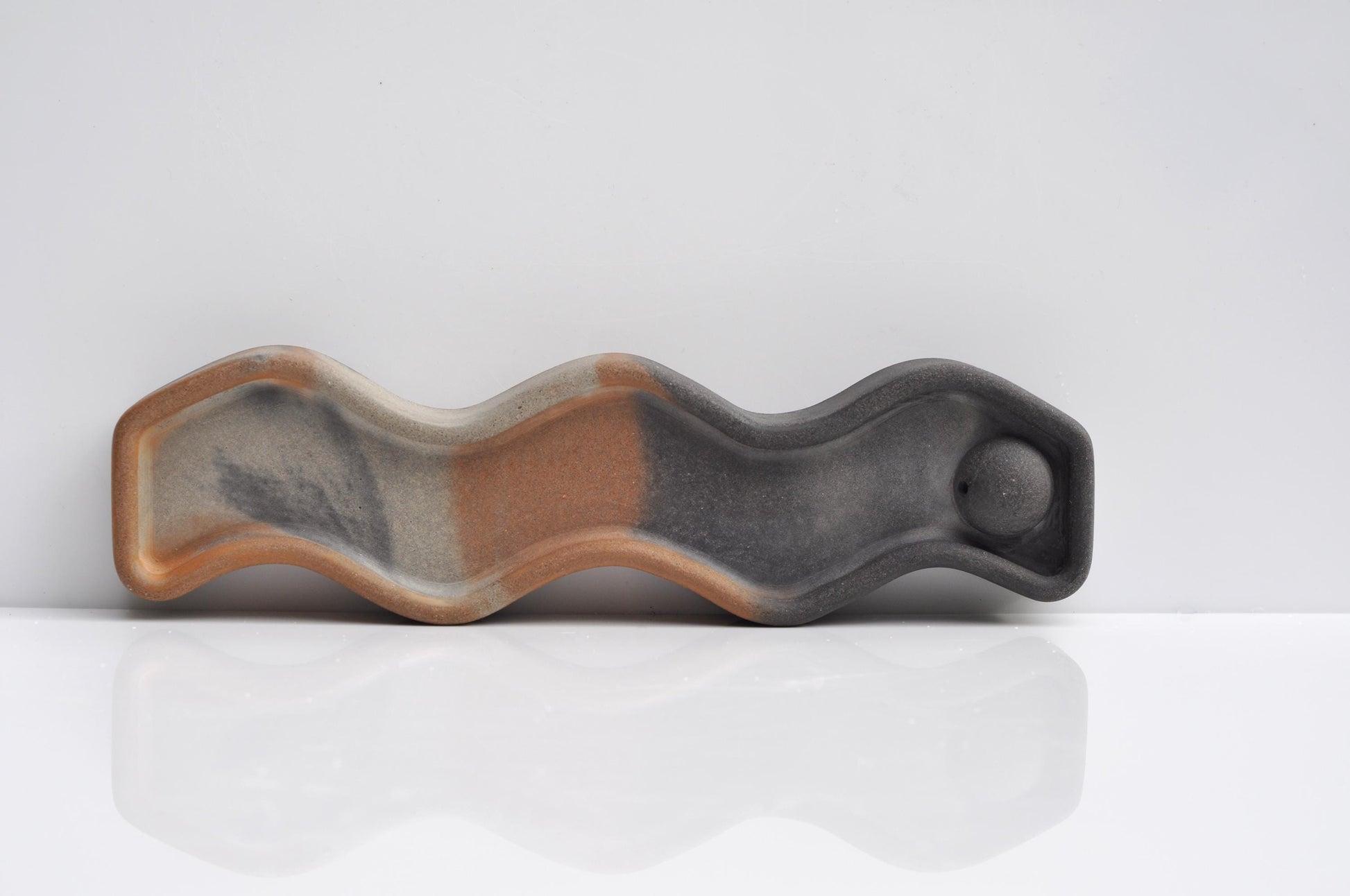 Wavy concrete dish with two-tone brown and gray design on a white background