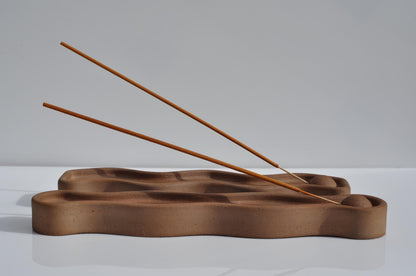 Wooden incense holder with two sticks on a white surface and gray background